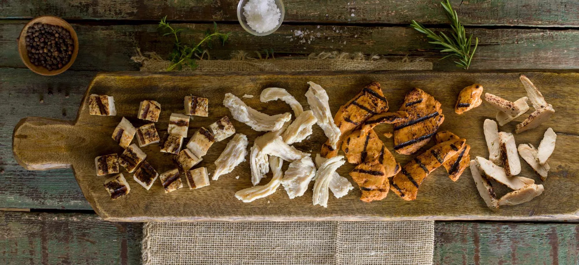 An assortment of BrucePac cooked protein cuts on a wooden serving board